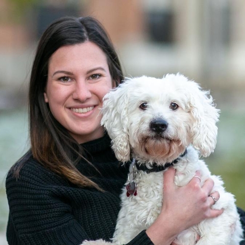 A girl wearing black holds a white cockapoo.